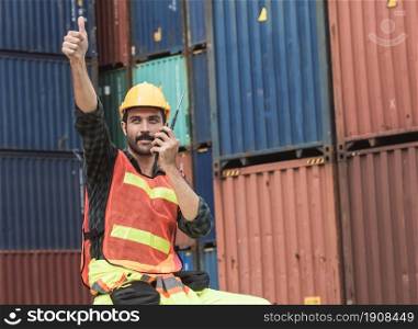 Caucasian beard foreman or Engineer wearing safety helmet and control for loading containers while talking on walkie talkie. Engineering and Shipping Concept.