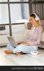 Caucasian blond woman with headphones and laptop on the sofa at home.. Caucasian blond woman with headphones and laptop on the sofa