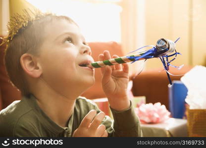 Caucasian boy at birthday party blowing noisemaker.