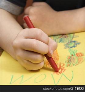 Caucasian boy drawing on yellow paper with crayons.