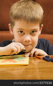 Caucasian boy drawing with crayons and looking at viewer.