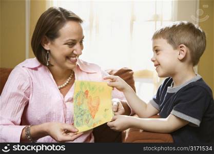 Caucasian boy giving mid adult mother a drawing.