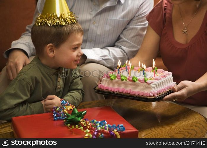 Caucasian boy in party hat with Birthday cake and family.