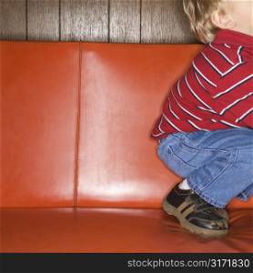 Caucasian boy kneeling on vinyl sofa.