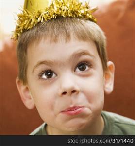 Caucasian boy wearing party hat making facial expression and looking at viewer.