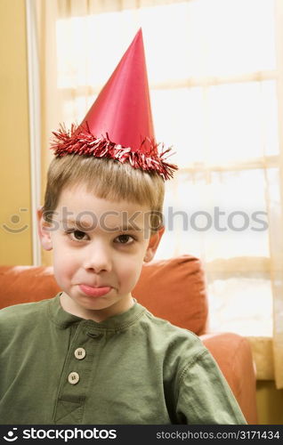 Caucasian boy wearing party hat pouting and looking at viewer.