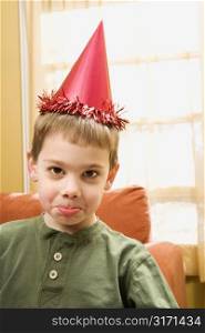 Caucasian boy wearing party hat pouting and looking at viewer.