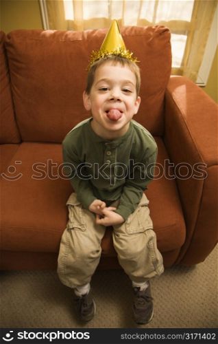 Caucasian boy with party hat looking at viewer and sticking out tongue.
