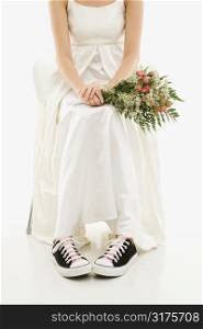 Caucasian bride holding bouquet exposing her tennis shoes.