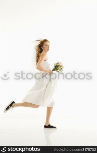 Caucasian bride running and holding bouquet.