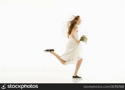 Caucasian bride running and holding bouquet.