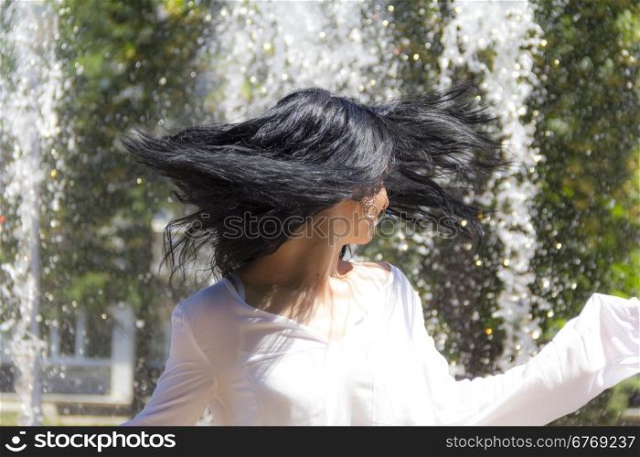 Caucasian brunette woman playing with hairs on fountain background