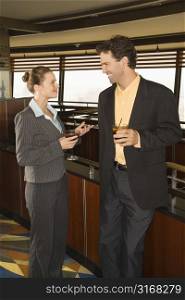 Caucasian business man and woman standing in bar with alcoholic beverages.