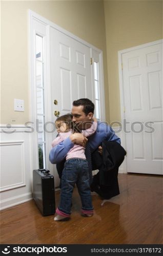 Caucasian businessman at door with briefcase hugging daughter.