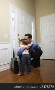 Caucasian businessman at door with briefcase hugging daughter.