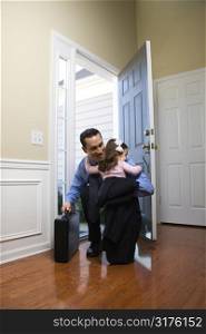 Caucasian businessman at open door with briefcase hugging daughter.