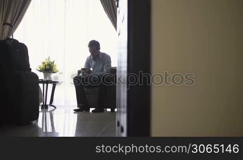 Caucasian businessman talking with mobile telephone in hotel room during business trip. Dolly shot
