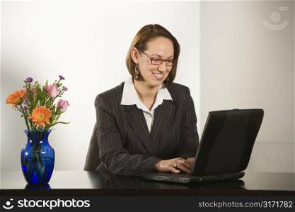 Caucasian businesswoman sitting at desk smiling with laptop computer.