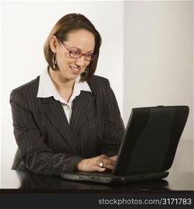 Caucasian businesswoman sitting at desk smiling with laptop computer.