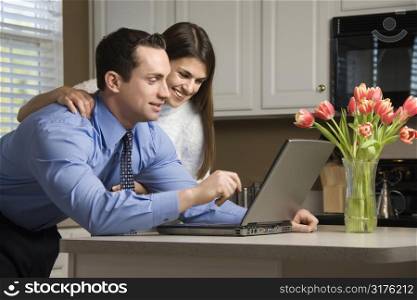 Caucasian couple in kitchen looking at laptop computer.