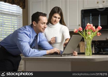 Caucasian couple in kitchen with coffee looking at laptop computer.