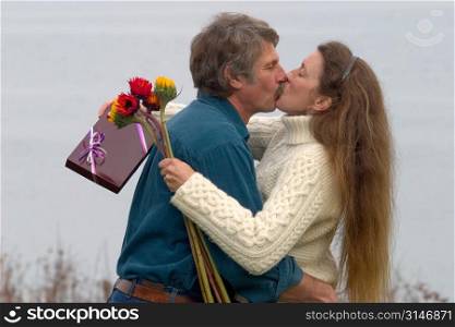 Caucasian Couple Kissing In Nature With Flowers And Chocolates