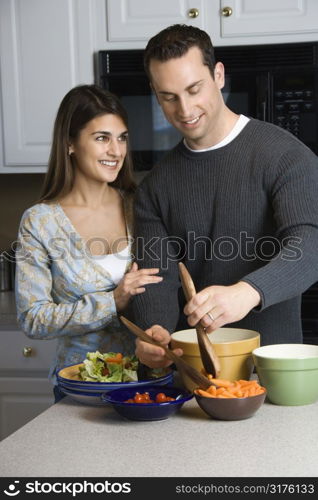 Caucasian couple making salad at kitchen counter.