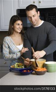 Caucasian couple making salad at kitchen counter.