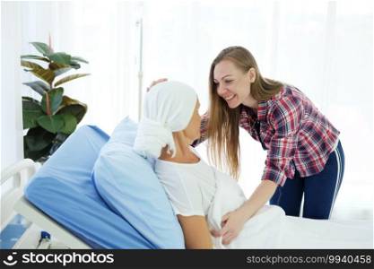 Caucasian daughter is talking and take care her Elderly Mother in white headscarf is laying on bed in hospital after chemotherapy because she is suffering from cancer or Leukemia patient.