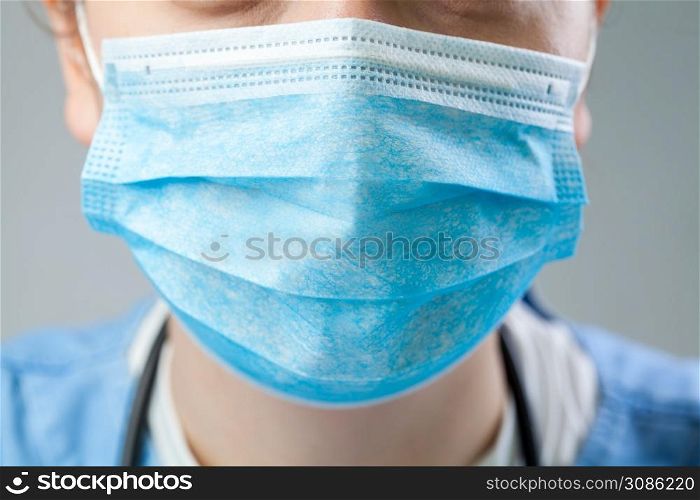 Caucasian doctor or nurse wearing blue protective surgical face mask, closeup detail, Coronavirus COVID-19 global pandemic crisis outbreak causing shortage of staff and personal protective equipment