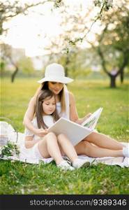 Caucasian family, mother and daughter together watching a family photo album in spring at a picnic in the garden, the concept of family values, generations and memories