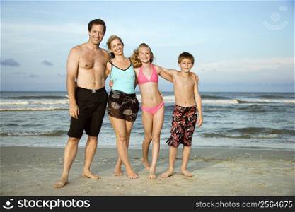 Caucasian family of four standing on beach.