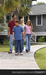 Caucasian family of four walking down suburban sidewalk with house in background.