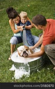 Caucasian family with toddler son giving English Bulldog a bath outdoors.