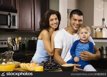 Caucasian family with toddler son in kitchen at breakfast smiling at viewer.