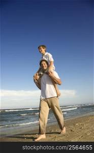 Caucasian father with pre-teen boy on shoulders on beach.