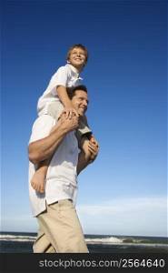 Caucasian father with pre-teen on shoulders on beach.