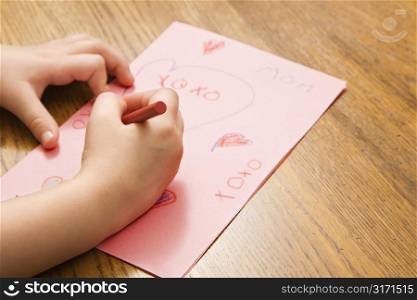 Caucasian female child hands drawing on paper with crayons.
