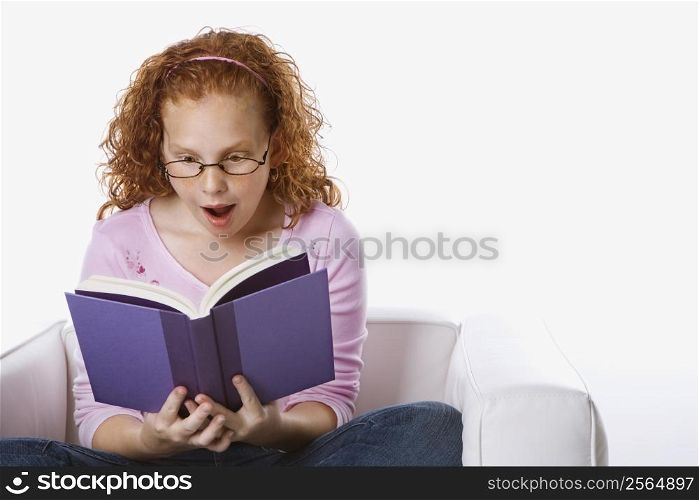 Caucasian female child sitting reading book looking surprised.