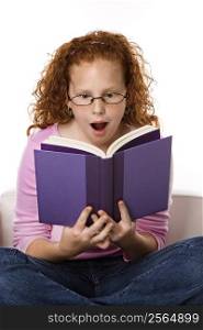 Caucasian female child sitting reading book looking surprised.