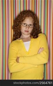 Caucasian female child with arms crossed wearing eyeglasses looking at viewer.