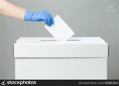 Caucasian female hand wearing blue protective latex rubber glove placing ballot paper in vote box,side view,prevention of spread & transfer of Coronavirus at the USA voting place, COVID-19 pandemic US