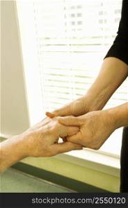 Caucasian female nurse massaging arthritic hands of elderly man at retirement community center.
