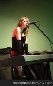 Caucasian female singing into a microphone and playing the keyboard.
