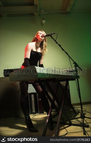Caucasian female singing into microphone and playing the keyboard.
