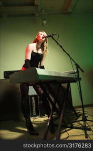 Caucasian female singing into microphone and playing the keyboard.