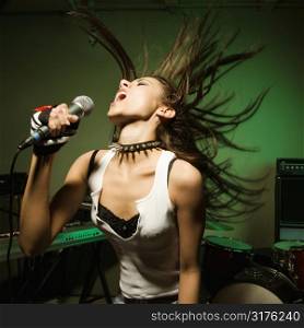 Caucasian female swinging head and hear while singing into microphone.
