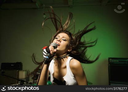 Caucasian female swinging head and hear while singing into microphone.