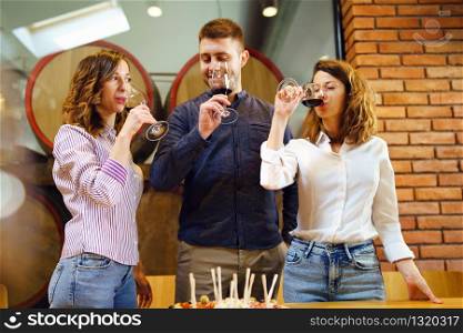 Caucasian friends two sisters or girlfriends and boyfriend with friend standing by the table at the restaurant or winery holding glasses of red wine drinking celebrating man looking to a girl