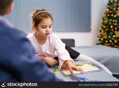 Caucasian girl four or five years old over the shoulder of her brother, sister playing at home on the sofa bed solving puzzles